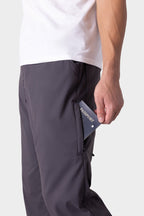 A person wearing 686 Men's Everywhere® Merino-Lined Pant - Relaxed Fit in dark color places a passport into the pant’s zippered side pocket. The image highlights the lower torso, showcasing the functionality and style of the 686 pants.