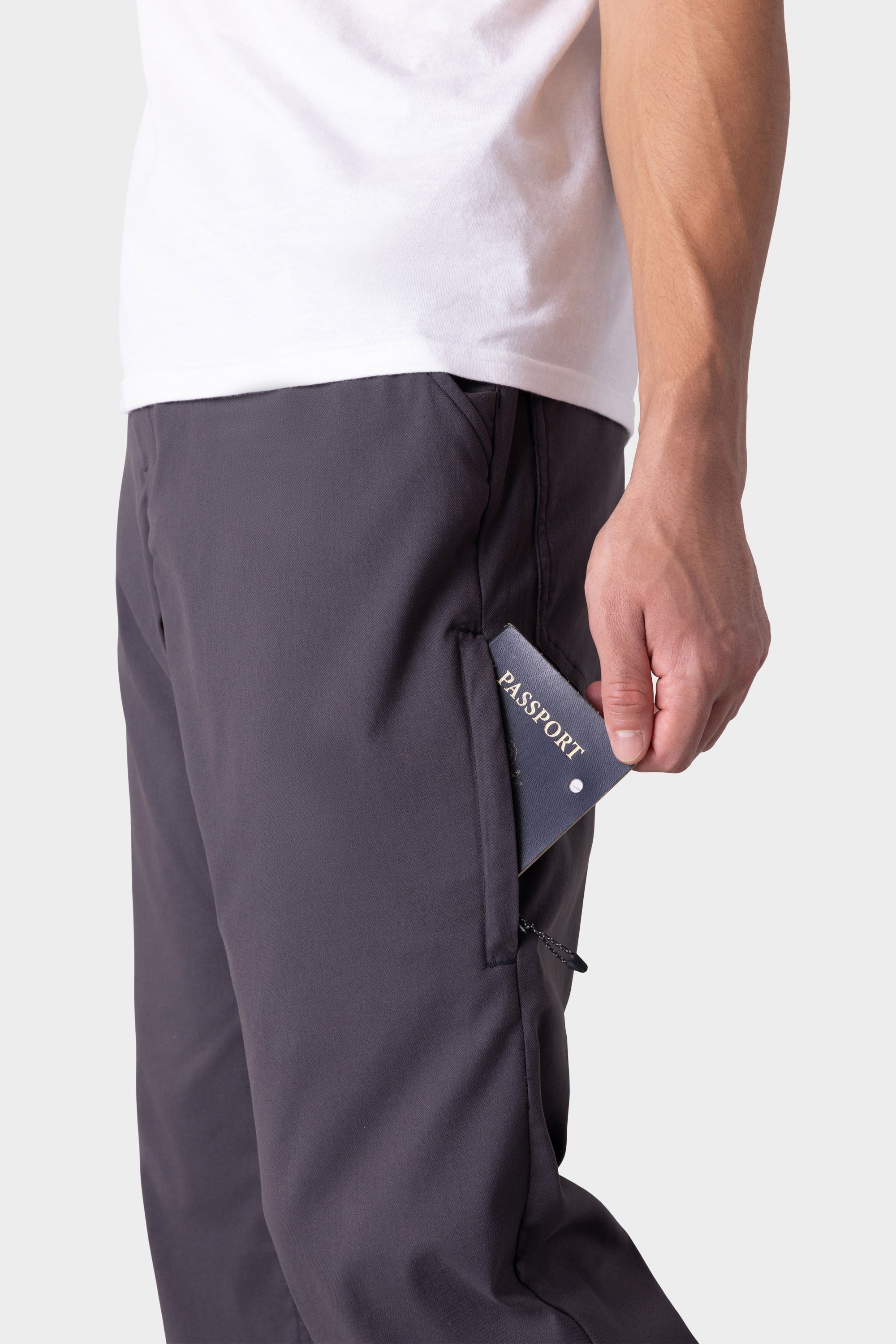 A person wearing 686 Men's Everywhere® Merino-Lined Pant - Relaxed Fit in dark color places a passport into the pant’s zippered side pocket. The image highlights the lower torso, showcasing the functionality and style of the 686 pants.