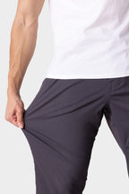 A person in a white shirt and dark pants stretches the fabric of the 686 Men's Everywhere® Merino-Lined Pant - Relaxed Fit, demonstrating the comfort and flexibility of these pants from 686.