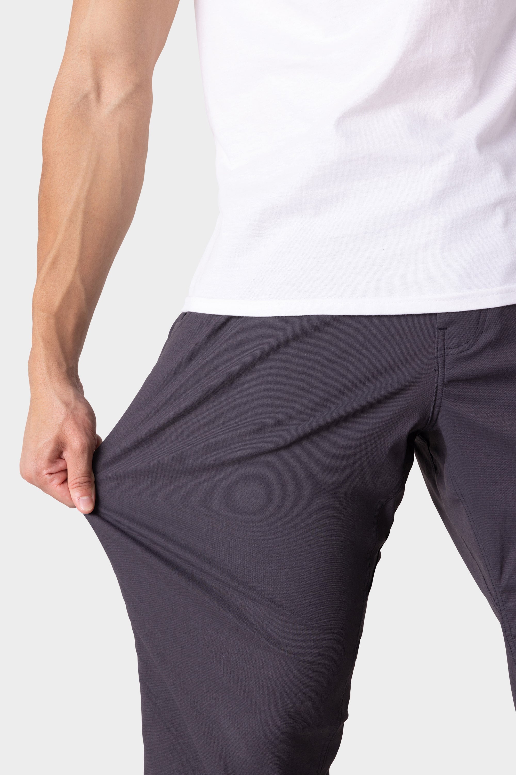 A person in a white shirt and dark pants stretches the fabric of the 686 Men's Everywhere® Merino-Lined Pant - Relaxed Fit, demonstrating the comfort and flexibility of these pants from 686.