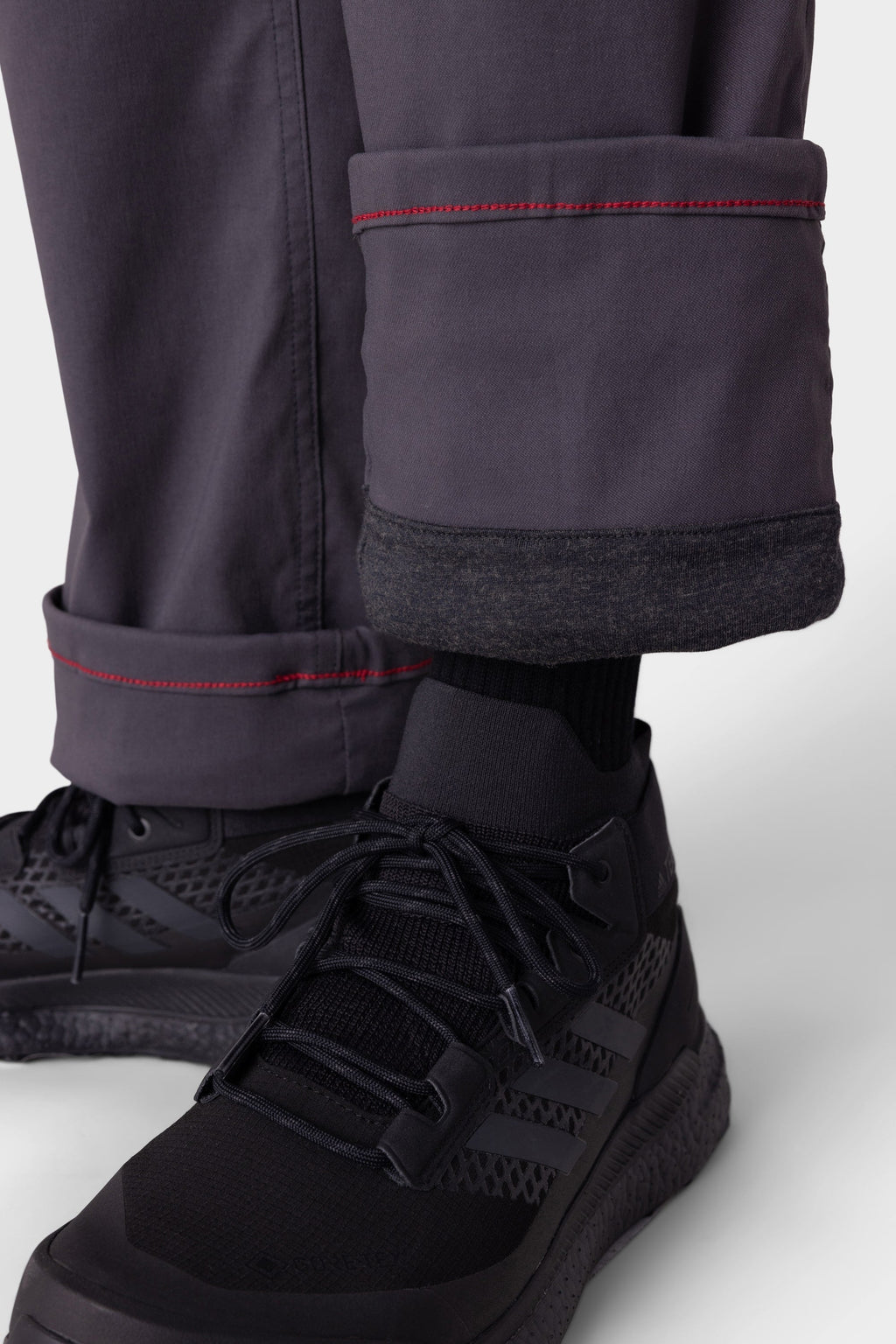 Close-up of a person wearing 686 Men's Everywhere® Merino-Lined Pant - Relaxed Fit. The dark gray pants feature red stitching and a cozy merino lining, ideal for staying warm and stylish when paired with insulated outerwear from 686.