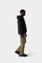 A person stands in profile against a plain light background, wearing a stylish black hooded jacket, black shoes, and 686 Men's Everywhere® Merino-Lined Pant - Relaxed Fit by 686.
