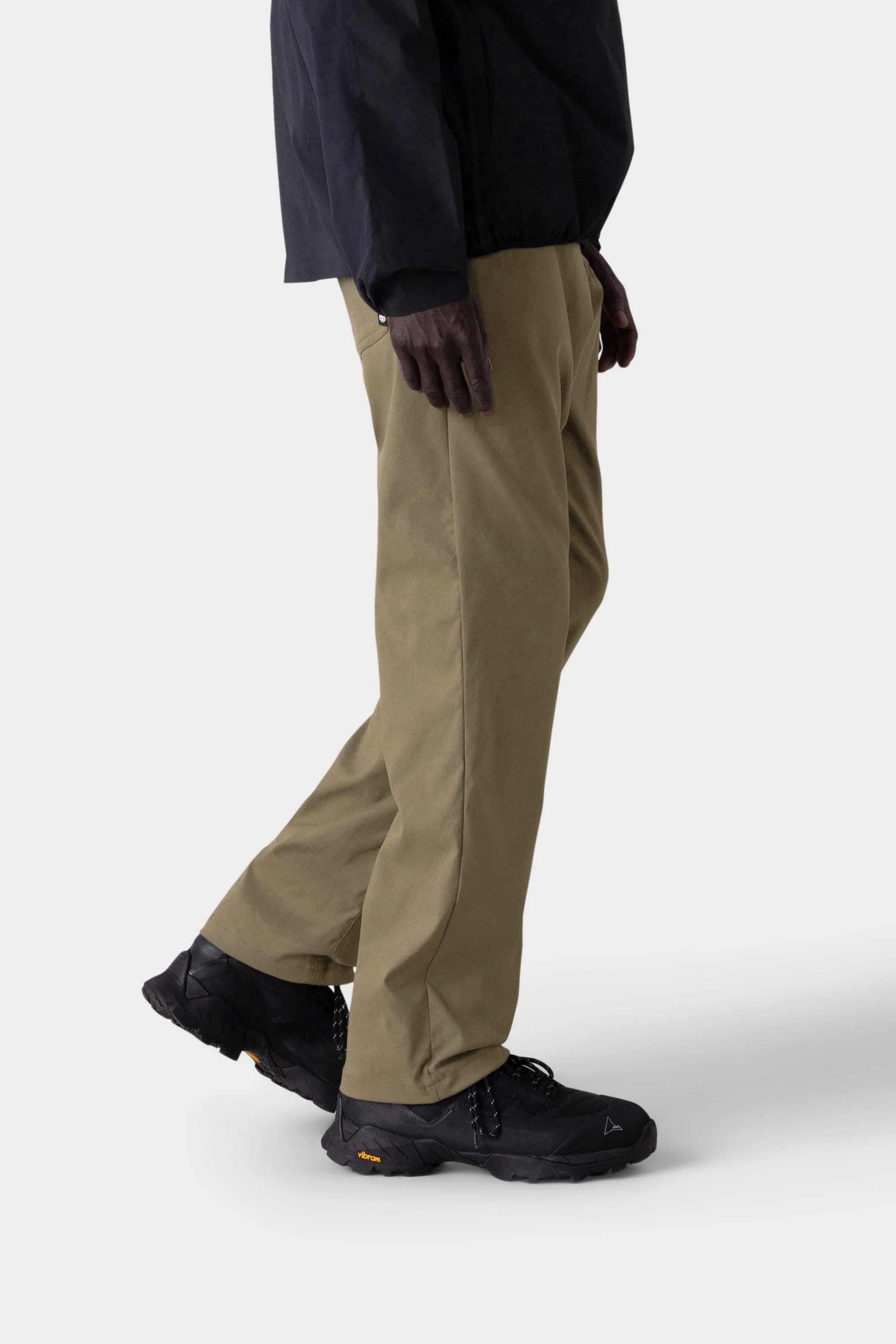 A person wearing 686 Men's Everywhere® Merino-Lined Pant - Relaxed Fit in light brown, a stylish insulated jacket, and black sneakers is walking against a plain light gray background, with only the lower half of the body visible.
