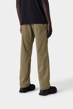 A person stands facing away in 686 Men's Everywhere® Merino-Lined Pant - Relaxed Fit, paired with a black shirt and black shoes, styled with insulated outerwear against a plain light gray background.