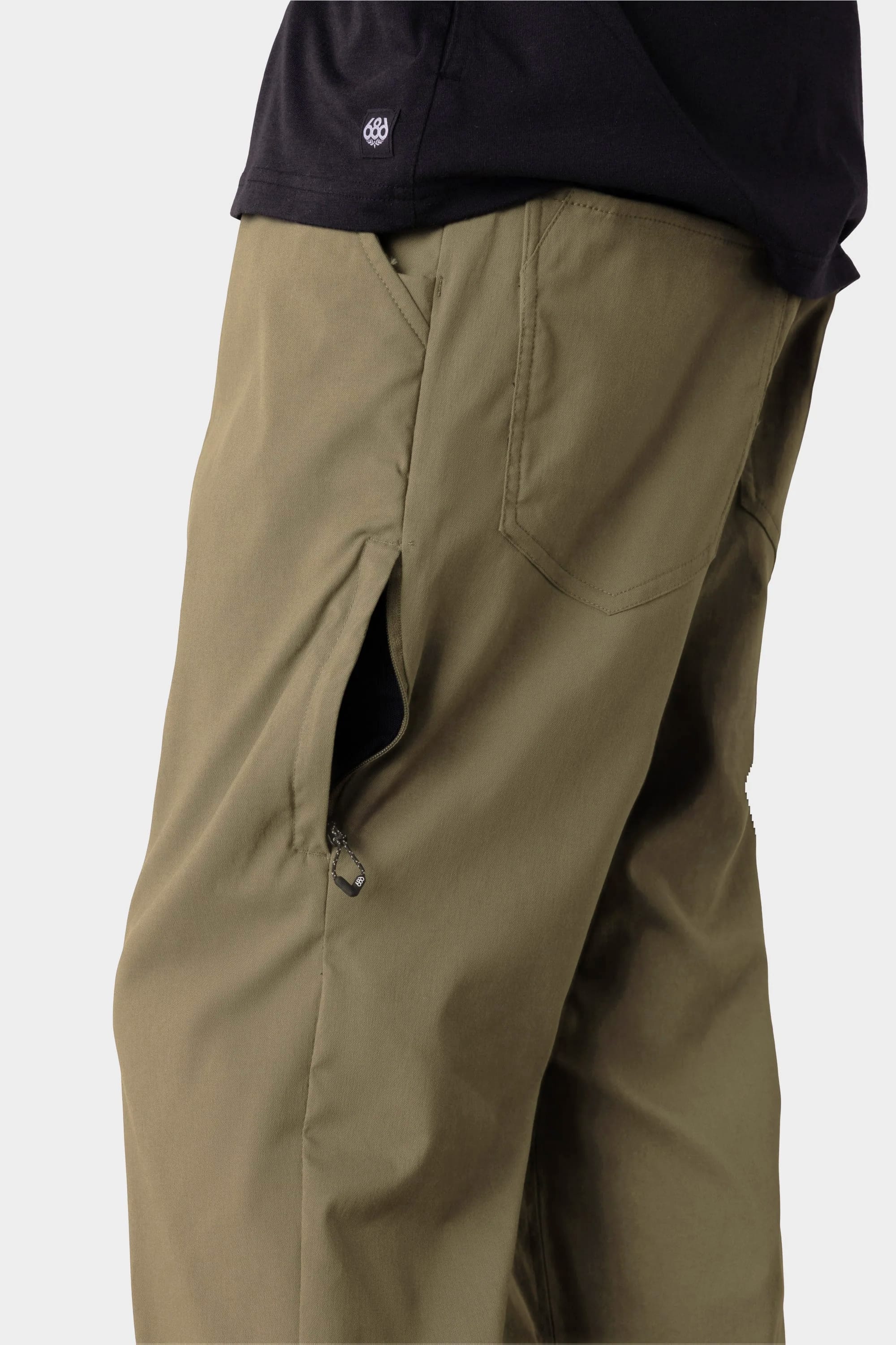 A person wearing 686 Men's Everywhere® Merino-Lined Pant - Relaxed Fit in olive green with a zippered side pocket and a black shirt, shown waist down against a plain background—ideal for pairing with 686's stylish insulated outerwear on chilly days.