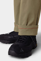 A close-up of a person wearing the 686 Men's Everywhere® Merino-Lined Pant - Relaxed Fit, featuring a rolled cuff with red stitching and paired with black hiking shoes and a warm jacket—ideal for stylish comfort on chilly days.