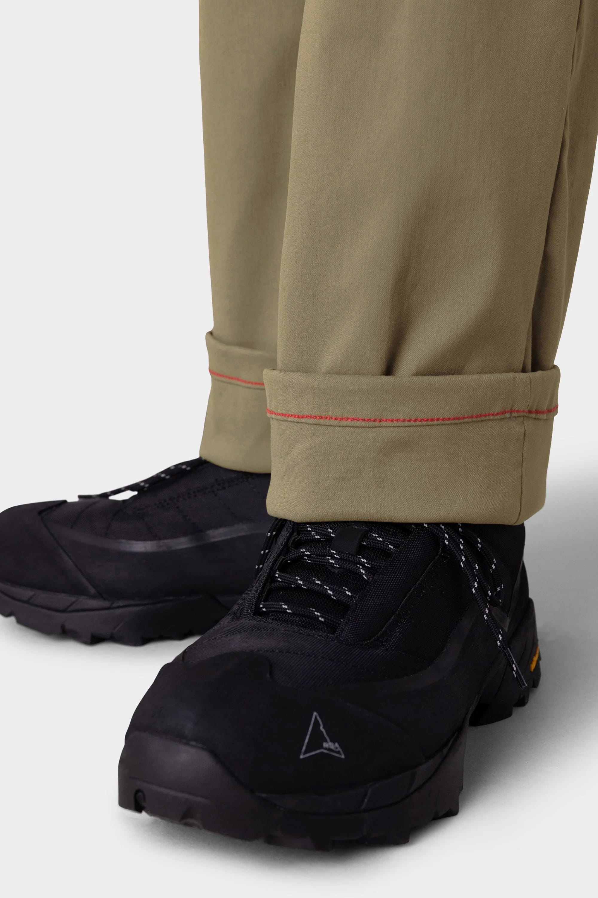 A close-up of a person wearing the 686 Men's Everywhere® Merino-Lined Pant - Relaxed Fit, featuring a rolled cuff with red stitching and paired with black hiking shoes and a warm jacket—ideal for stylish comfort on chilly days.