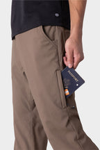 Wearing the 686 Men's Everywhere® Merino-Lined Pant - Relaxed Fit, a person puts a navy passport into a zippered side pocket, with their torso and arm visible against a plain light background.