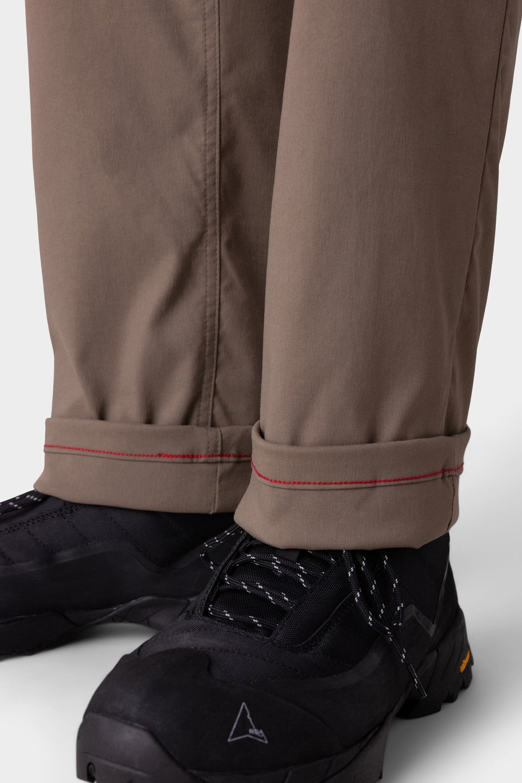 Close-up of lower legs in 686 Men's Everywhere® Merino-Lined Pant - Relaxed Fit, featuring brown fabric with red-stitched cuffs and paired with black hiking shoes—perfect for pairing with insulated outerwear on outdoor adventures.