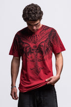 A person with curly dark hair looks down wearing the 686 Affliction Death Eyes SS Tee in red by 686, featuring black wings, a cross, and bold text, paired with black pants against a plain light background.