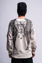 A person wearing a black beanie and the 686 Affliction Death Eyes Thermal LS by 686, a light-colored long-sleeve men's t-shirt featuring large, detailed black angel wings and a cross design on the back, stands with their back to the camera.