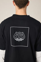 A person shown from behind wears the 686 Wordmark Relaxed 2fer LS Tee, a black 100% cotton men’s t-shirt by 686, featuring a white outlined square with the 686 logo and graphic design on the back, complementing their short brown hair.