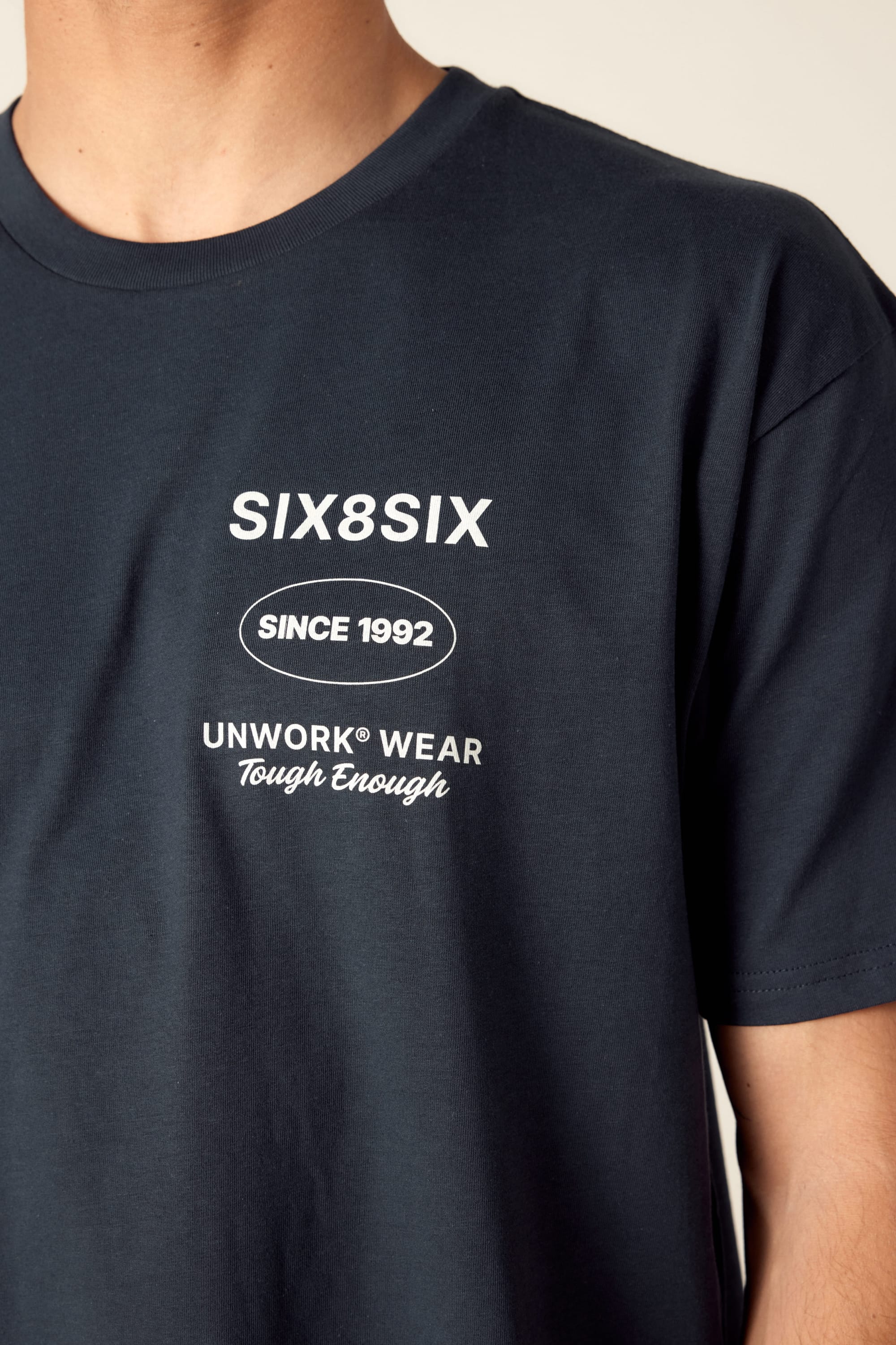 A person wearing a dark blue 686 Unwork Wear Authentic S/S Tee by 686, featuring white chest text: SIX8SIX, SINCE 1992, and UNWORK WEAR Tough Enough. Only the upper torso is shown.