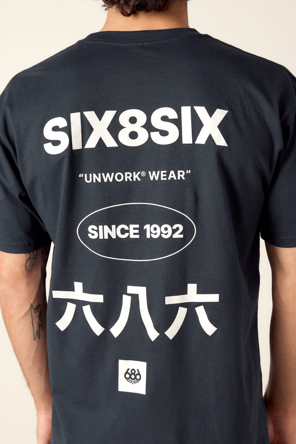 A person wearing the 686 Unwork Wear Authentic S/S Tee in mens black cotton, featuring white SIX8SIX, UNWORK WEAR, SINCE 1992, 六八六 text on the back and a small circular logo at the bottom. Brand: 686.