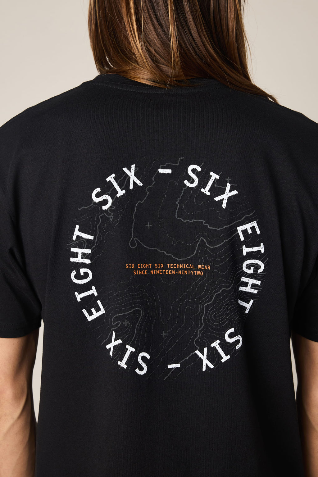 A person wearing the 686 Lifts Authentic SS Tee by 686—a black 100% cotton men's t-shirt featuring a topographic map graphic on the back and circular SIX EIGHT SIX text, plus orange "TECHNICAL WEAR SINCE NINETEEN-NINETY TWO.