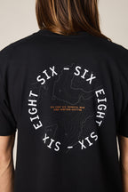 A person wearing the 686 Lifts Authentic SS Tee by 686—a black 100% cotton men's t-shirt featuring a topographic map graphic on the back and circular SIX EIGHT SIX text, plus orange "TECHNICAL WEAR SINCE NINETEEN-NINETY TWO.