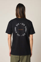 A person with long hair, seen from behind, wears the 686 Lifts Authentic SS Tee— a black 100% cotton t-shirt by 686 featuring a white “SIX EIGHT SIX” circle logo and subtle central graphic—paired with green pants.