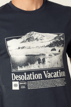 A person wearing the 686 Desolation Vacation Authentic S/S Tee—a dark 100% cotton mens T-shirt by 686 featuring a black-and-white mountain and lake landscape graphic with Desolation Vacation text.