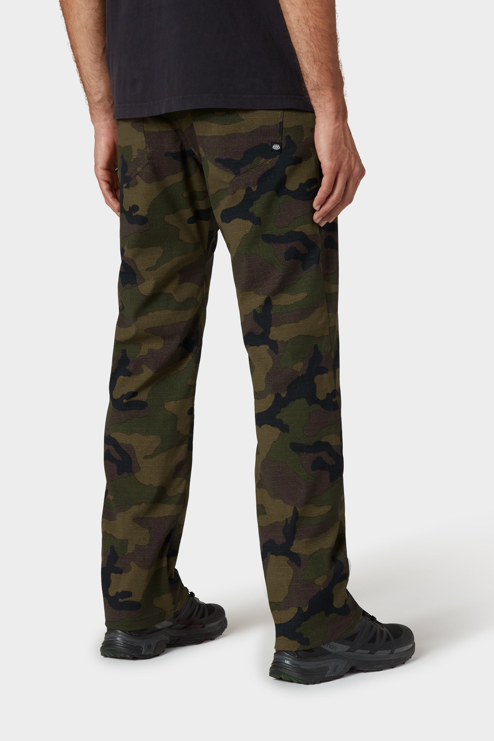 A person stands facing away in 686 Men's Everywhere® Merino-Lined Pant - Relaxed Fit, black shoes, a black t-shirt, and a stylish insulated jacket, all set against a plain white background.