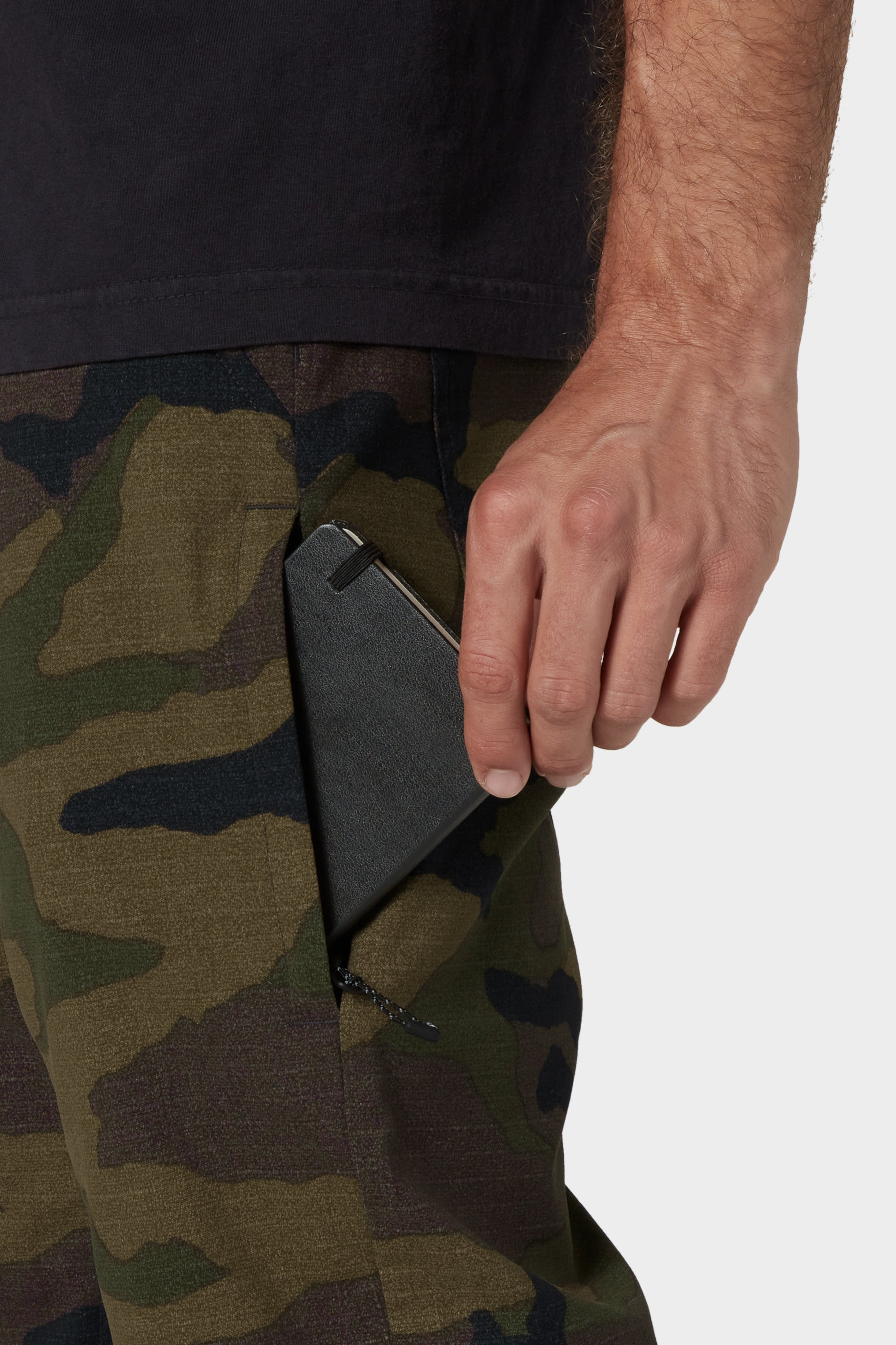 A person wearing 686 Men's Everywhere® Merino-Lined Pant - Relaxed Fit slips a black wallet into a zippered side pocket. Only their hand, arm, and the pant pocket are visible. Brand: 686.