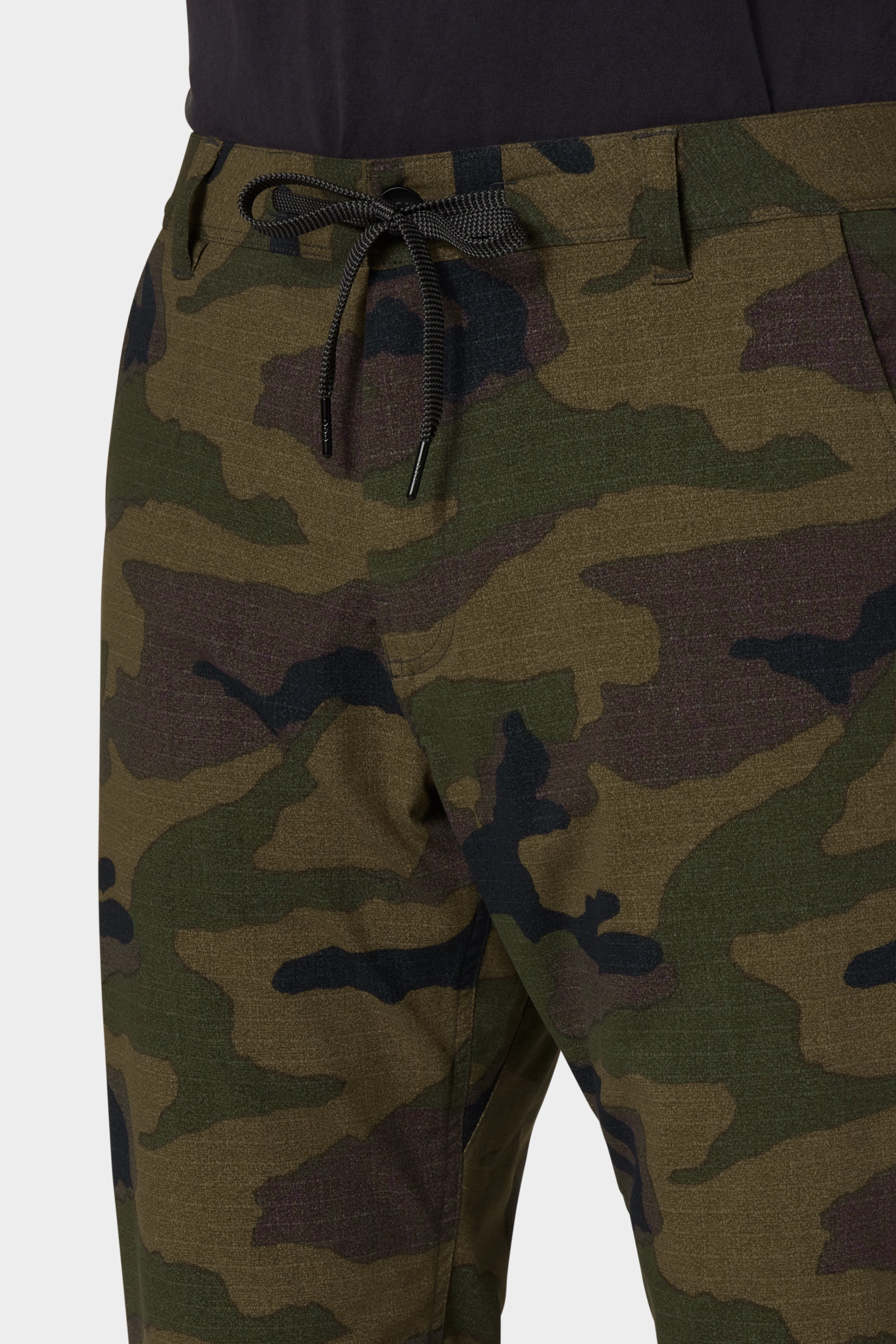 Close-up of a person wearing 686 Men's Everywhere® Merino-Lined Pant - Relaxed Fit in camo, paired with a dark shirt and insulated jacket. Only the waist and upper legs are visible. Brand: 686.
