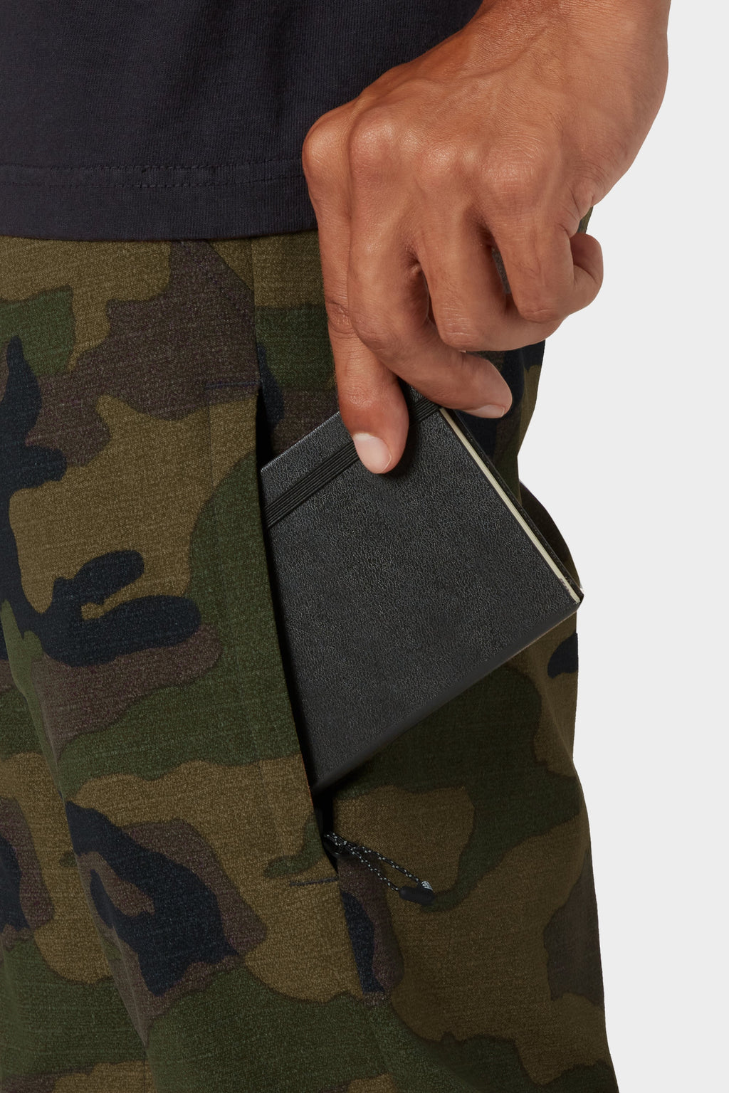 Wearing 686 Men's Everywhere® Merino-Lined Pant - Slim Fit, a person slides a black notebook into a side pocket, ready to stay warm and prepared in colder weather.