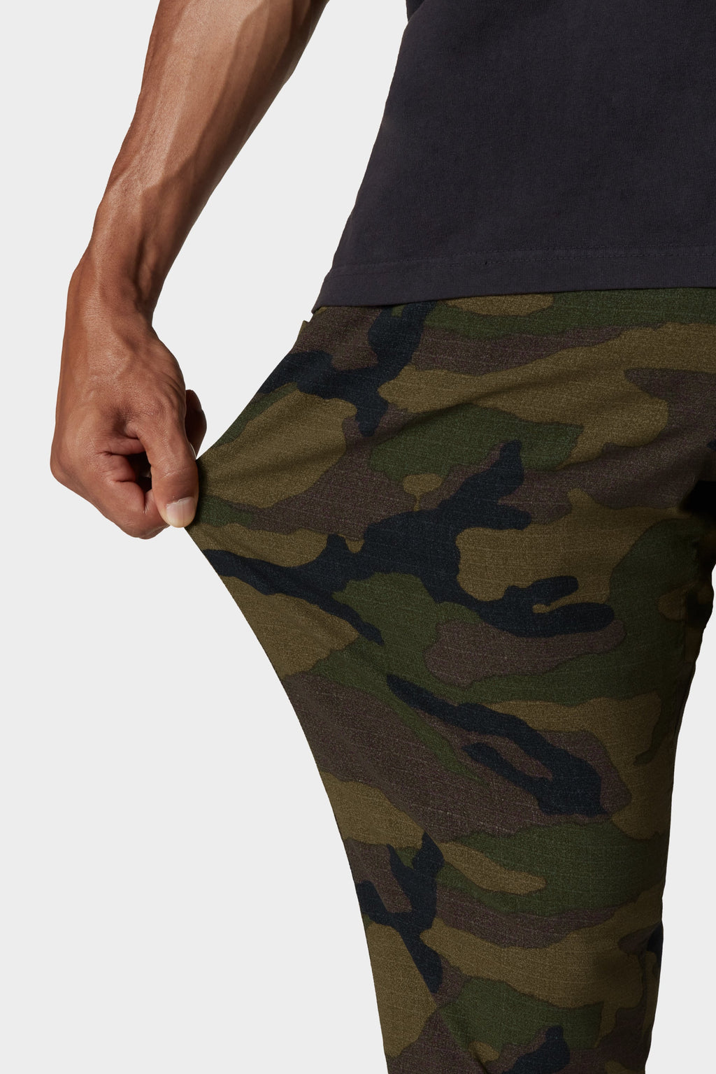 A person stretches the fabric of their 686 Men's Everywhere® Merino-Lined Pant - Slim Fit, revealing its comfort and flexibility—ideal for cold weather. Only their torso, hand, and part of the green camo pants are visible above a dark shirt.