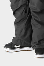 A close-up of a person wearing the 686 Men's SMARTY® 3-in-1 Cargo Pant with removable sweatpant liner, paired with black and white Nike sneakers with gum soles, standing on a light gray background—offering three ways to wear.