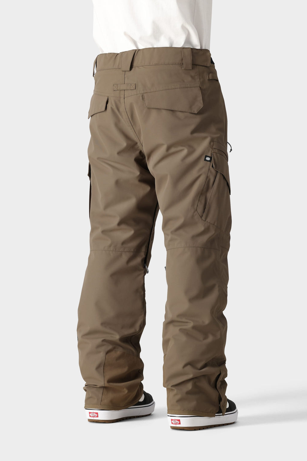 Seen from the back against a light gray background, a person wears 686 Men's SMARTY® 3-in-1 Cargo Pant in khaki brown with black Vans sneakers; these versatile cargo pants by 686 offer three ways to wear, plus multiple pockets and belt loops.
