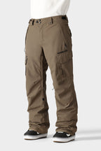 A person in loose-fitting 686 Men's SMARTY® 3-in-1 Cargo Pant with removable liner and multiple pockets, paired with black-and-white sneakers, stands against a plain light gray background.
