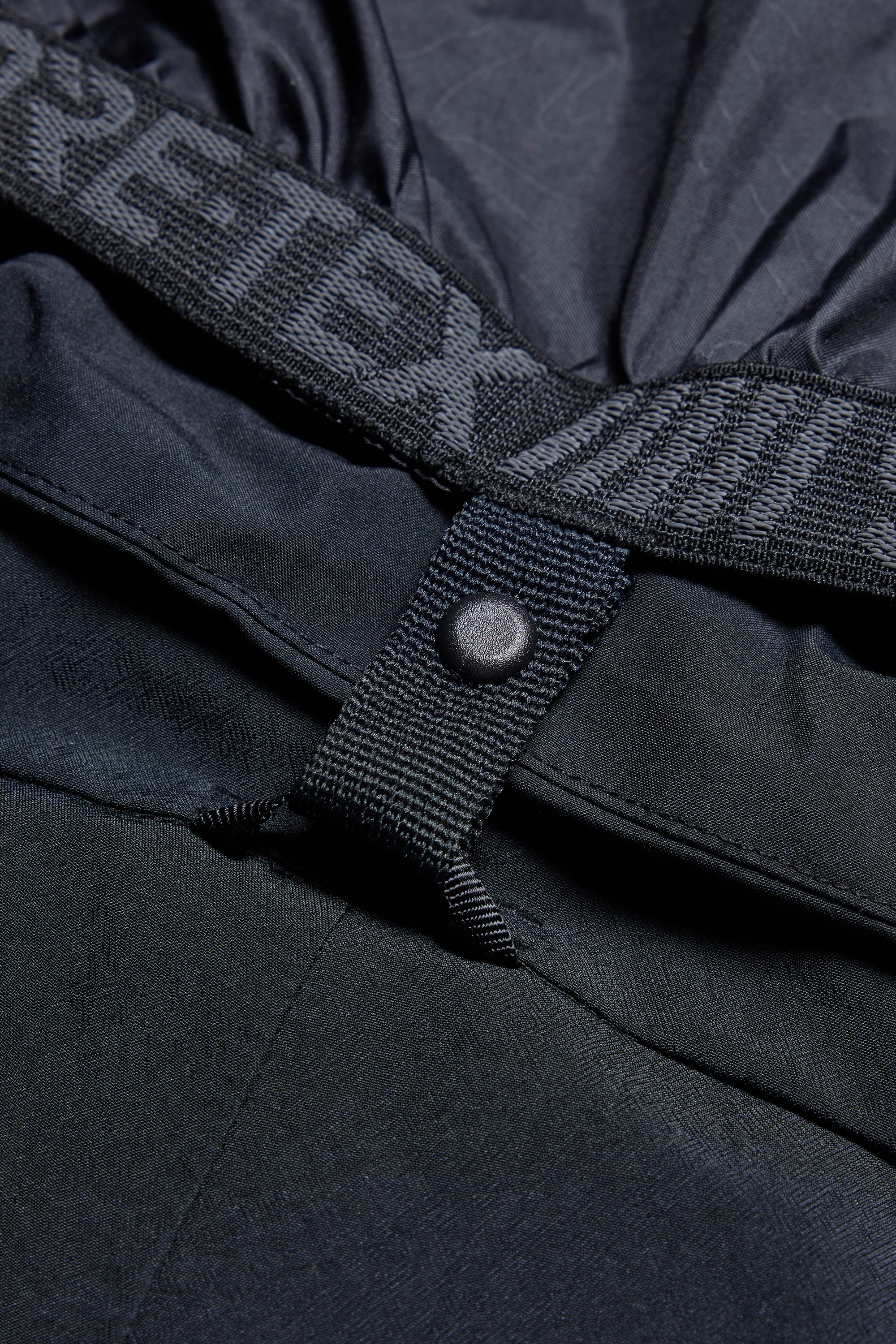 Close-up of the 686 Men's SMARTY® 3-in-1 Cargo Pant shows its black color, snap button, fabric loop, elastic waistband with partial GORE-TEX branding, and detailed stitching—highlighting its versatile three-way wear options.