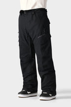 Only the lower half is visible: a person wearing 686 Men's SMARTY® 3-in-1 Cargo Pant—loose-fitting black cargos with multiple pockets and a removable sweatpant liner—paired with black-and-white sneakers against a light gray background.