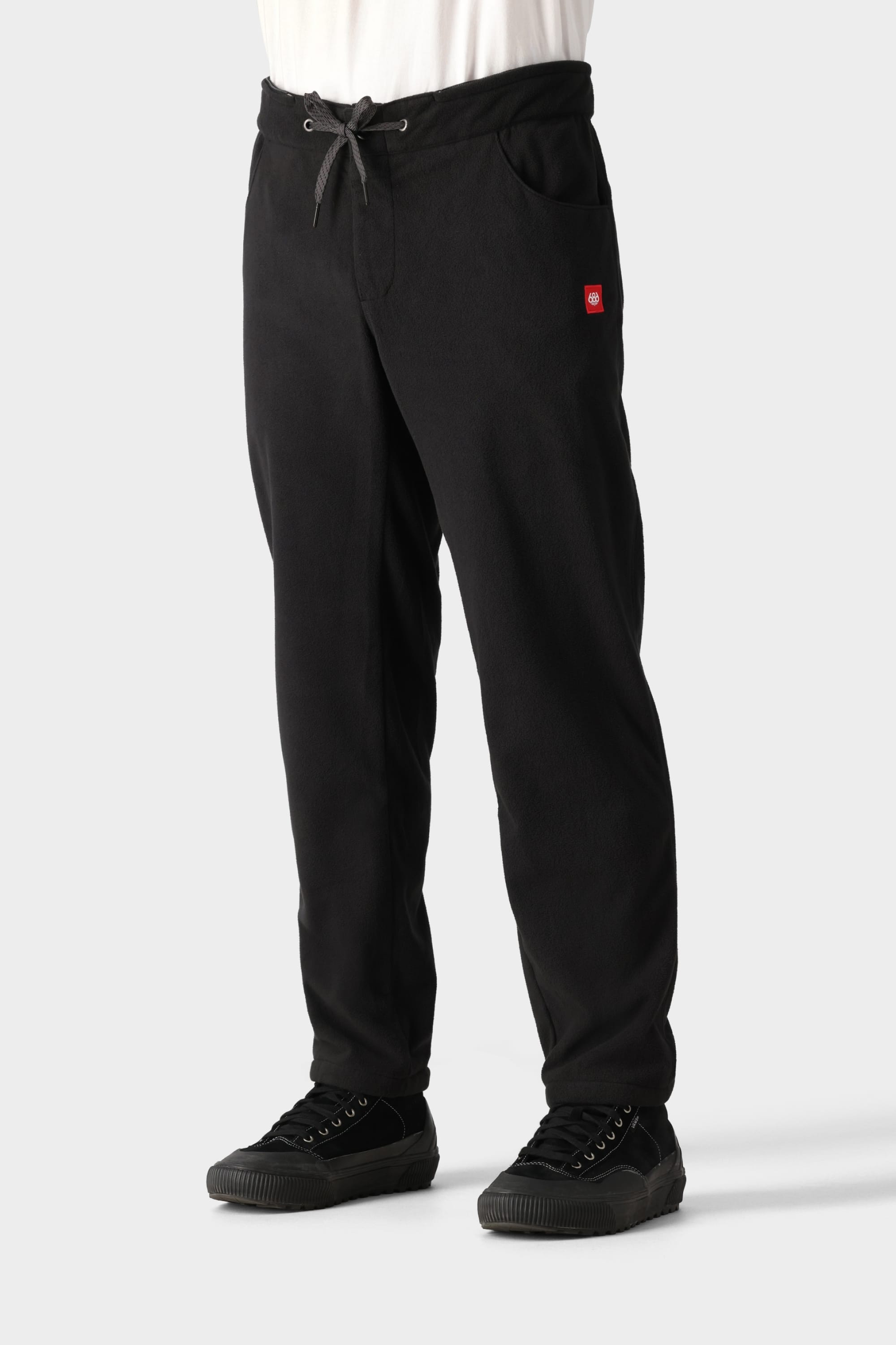 A person wears the 686 Men's SMARTY® 3-in-1 Cargo Pant with side pockets and a small red logo, paired with black sneakers and a white shirt. The pants feature a drawstring waist and three wear options. Background is plain light gray. Brand: 686.