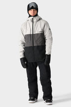 A person in a gray and black winter jacket, 686 Men's SMARTY® 3-in-1 Cargo Pant by 686, black gloves, snow boots, helmet, and ski goggles stands against a plain light background—showing three ways to wear the 3-in-1 cargo pant.