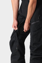 A person unzips a side vent on black 686 Men's SMARTY® 3-in-1 Cargo Pants, revealing mesh lining beneath. Only their lower torso and arms are shown against a plain background.