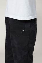 A person shown from the waist down wears a white shirt and 686 Men's Everywhere® Pant - Slim Fit in black camo, highlighting the side pocket with a small white 686 logo.