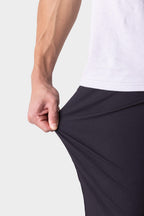 A person in a white shirt stretches the fabric of their 686 Men's Everywhere® Pant - Slim Fit, highlighting its elasticity, with just their torso and hand visible.