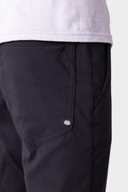 Close-up of 686 Men's Everywhere® Pant - Slim Fit, showing a breathable fabric, side pocket, and black and white logo tag, paired with a light shirt. Focus is on the upper area and pocket details.