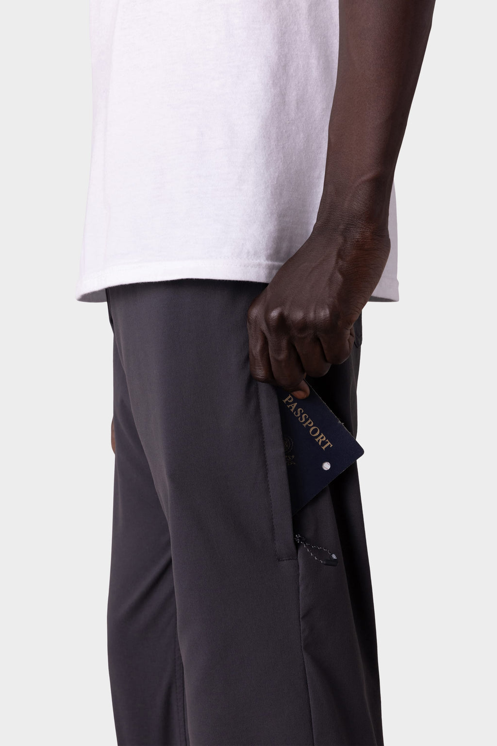 A person in a white shirt and 686 Men's Everywhere® Pant - Slim Fit is sliding a navy passport into the side zipper pocket, with focus on their hand, the pocket, and passport.