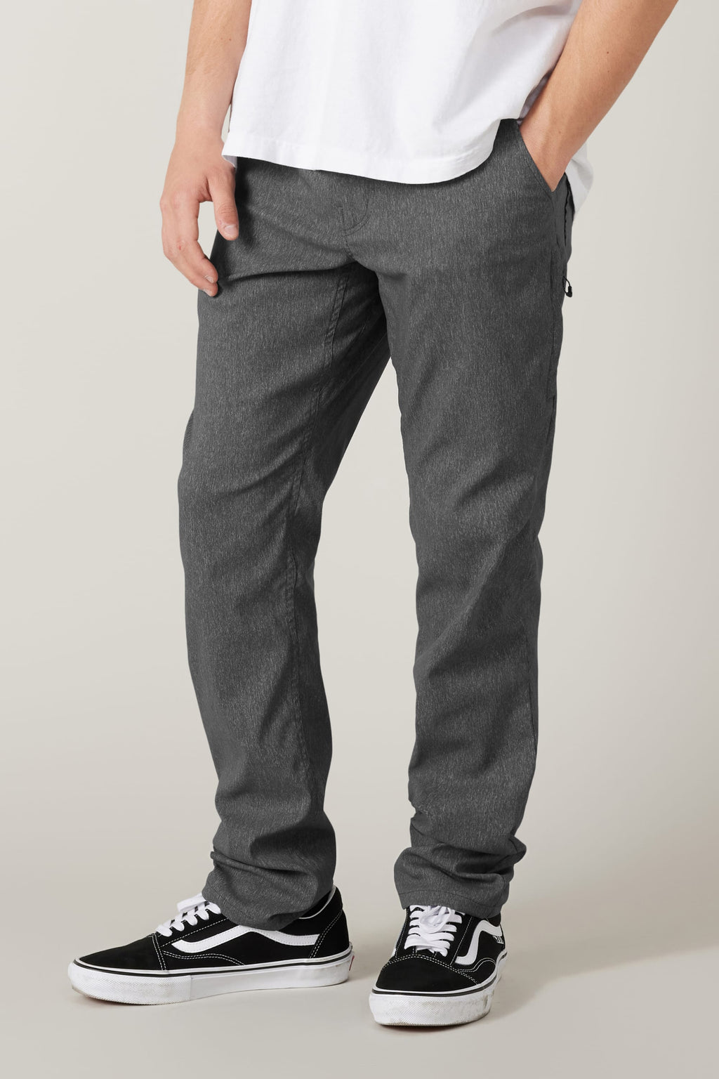 A person, only the lower half visible, stands against a plain light background wearing a white t-shirt, black-and-white Vans sneakers, and 686 Men's Everywhere® Pant - Slim Fit in stain-resistant gray.