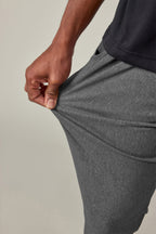 A man in black shirt stretches the fabric of the 686 Men's Everywhere® Pant - Slim Fit, showing off the pants' impressive flexibility and breathability.