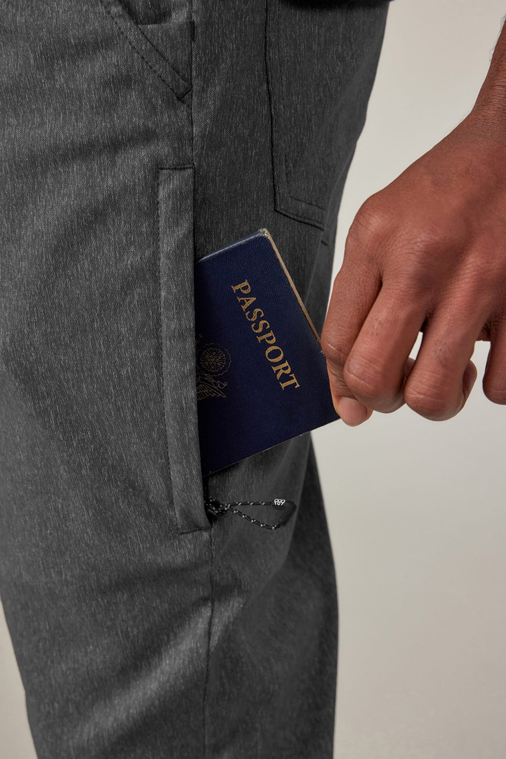 A person’s hand places a blue passport into the front pocket of 686 Men's Everywhere® Pant - Slim Fit by 686.