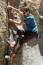 A man climbing a rock in 686 Men's Everywhere® Pant - Slim Fit by 686, designed for breathability and ideal for active adventures.