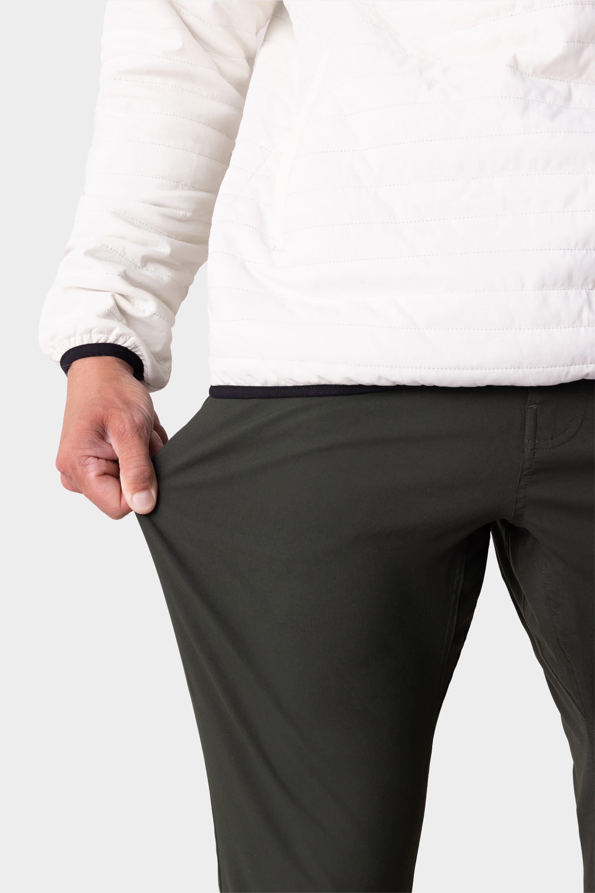 A person wearing a white jacket and dark pants uses one hand to stretch the fabric of their 686 Men's Everywhere® Pant - Slim Fit, highlighting the stretch and comfort of this breathable 686 style.