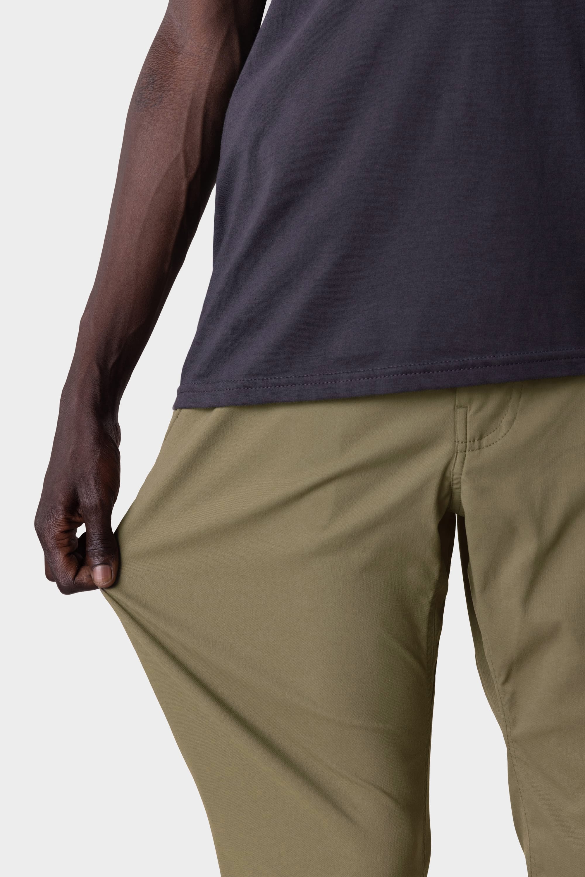 A person wearing the 686 Men's Everywhere® Pant - Slim Fit in olive green stretches the fabric of these stain-resistant pants, highlighting their flexible feel and breathable comfort.