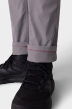 A close-up shows someone wearing 686 Men's Everywhere® Pant - Slim Fit in gray, cuffs rolled to display a red stitch detail. The breathable 686 pants are paired with black athletic sneakers.