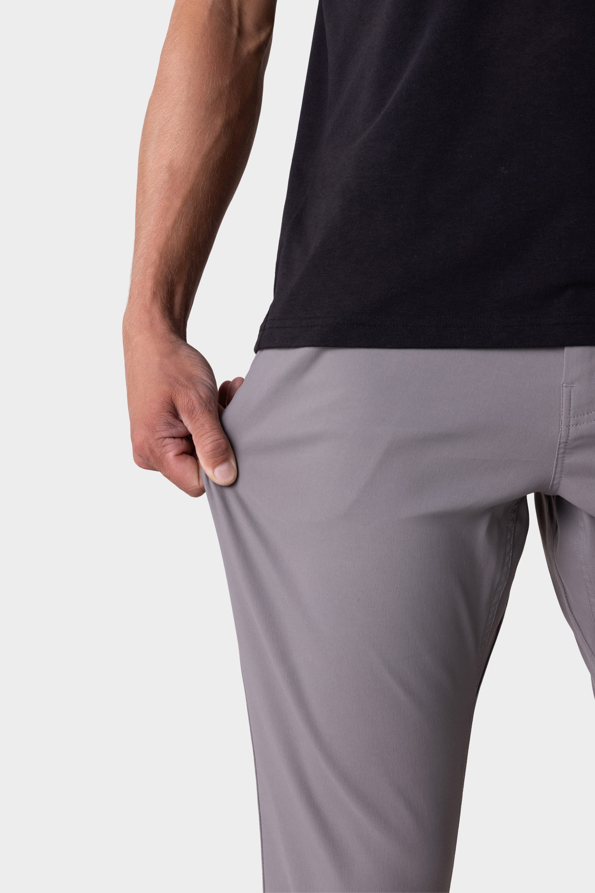 A person in 686 Men's Everywhere® Pant - Slim Fit in light gray and a black shirt stretches the fabric with one hand, showing the flexibility and breathability of these 686 pants.