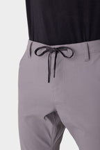 Close-up of a person wearing the 686 Men's Everywhere® Pant - Slim Fit in light grey with a black drawstring belt and a tucked-in black shirt, highlighting the waist and upper legs.