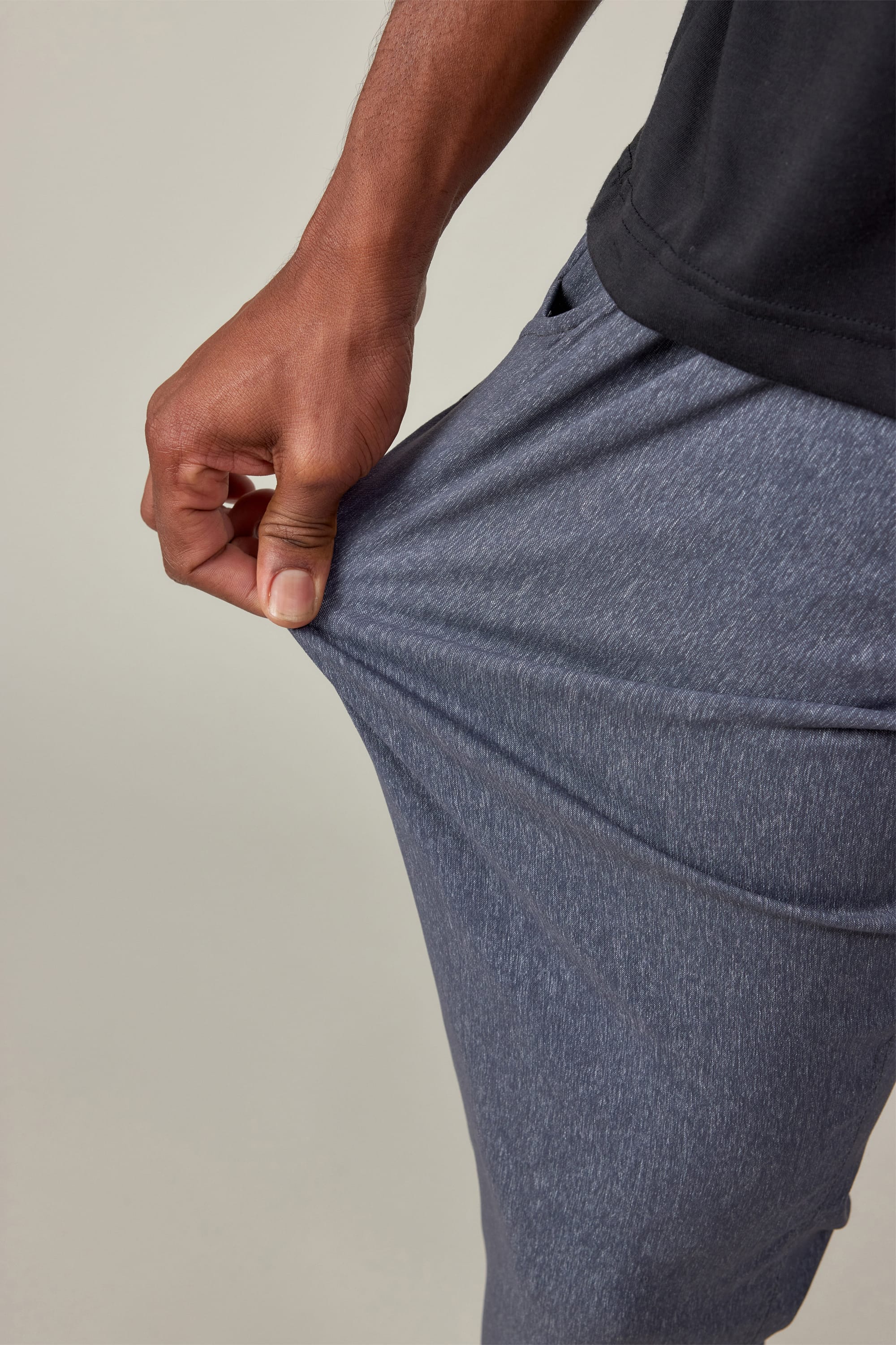 A person wearing 686 Men's Everywhere® Pant - Slim Fit in heathered blue and a black shirt stretches the fabric with their left hand, showcasing the pant’s impressive flexibility and stain-resistant material.