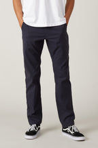 A person wearing a white t-shirt, 686 Men's Everywhere® Pant - Slim Fit by 686, and black sneakers with white laces stands with hands in pockets against a plain background.